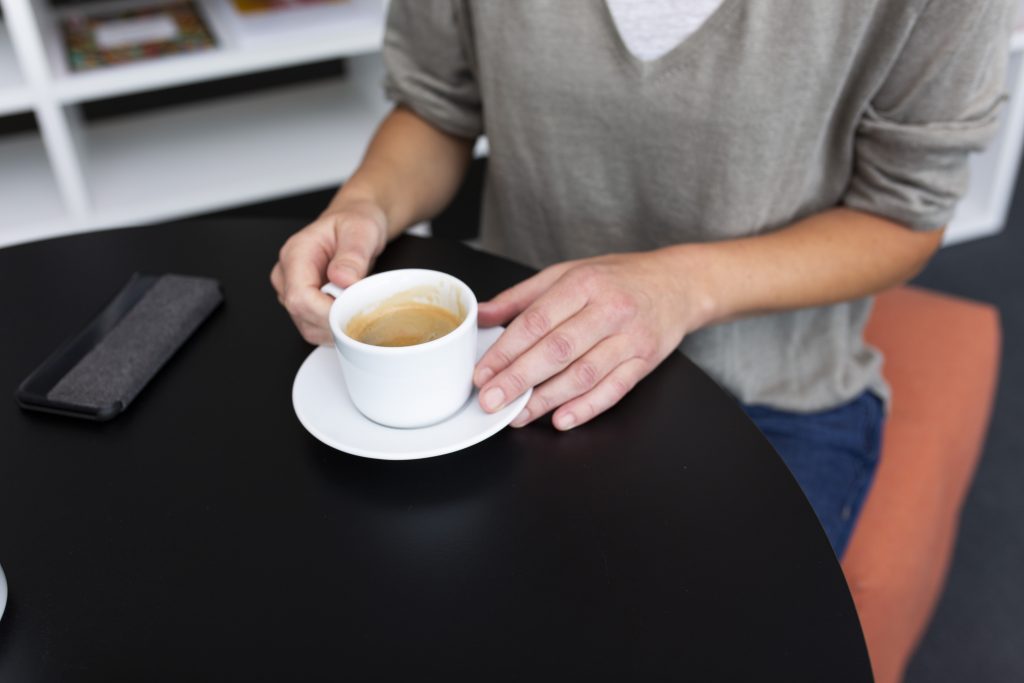 Hände halten eine Tasse Kaffee, die auf einem schwarzen Tisch steht