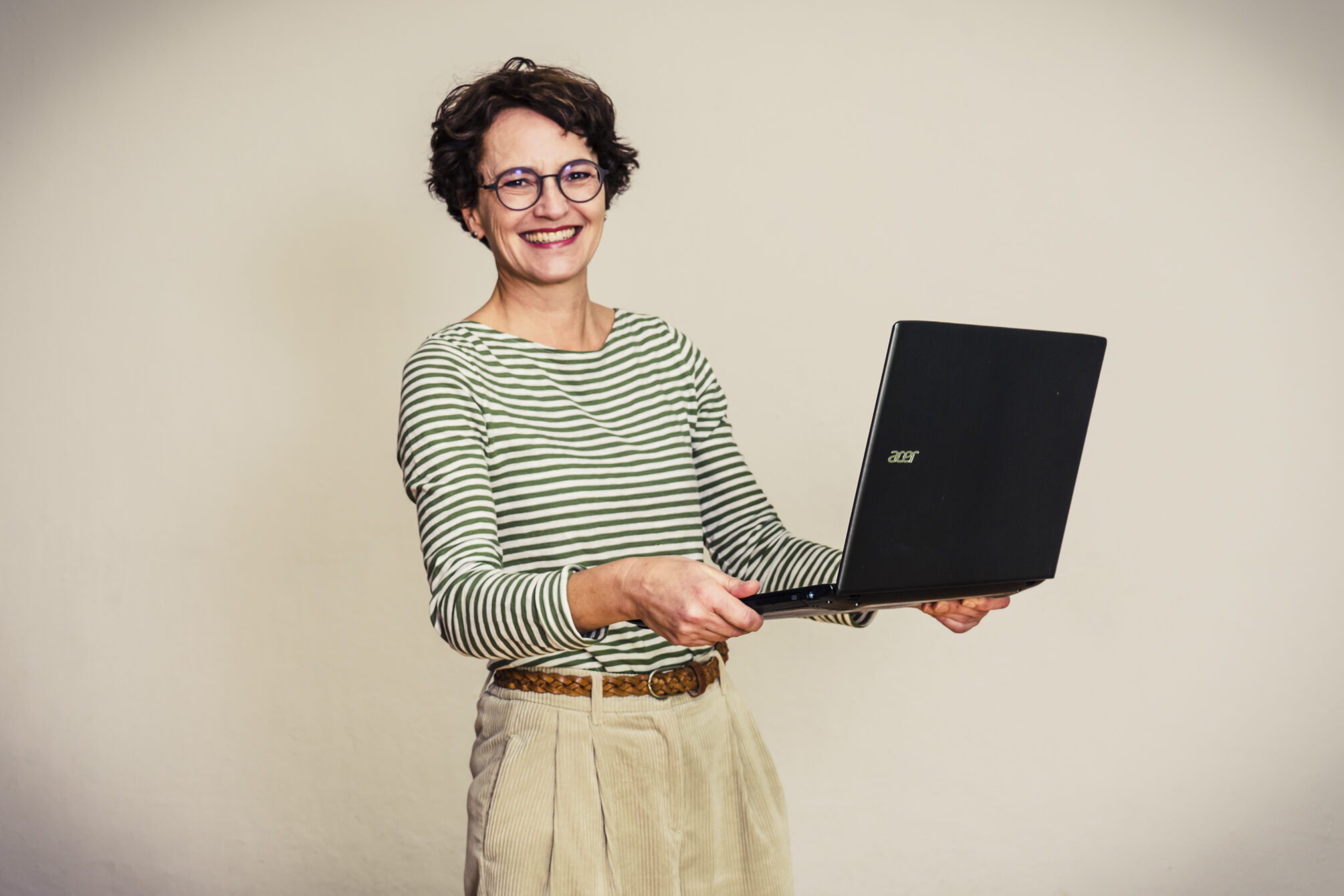 Frau mit Laptop, schaut fröhlich in die Kamera