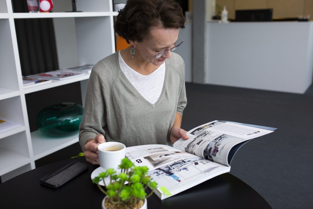 Erfolgreich Bloggen: Eva Dragosits sitzt mit einem Kaffee in einem Co-Working Space und liest in einem Magazin