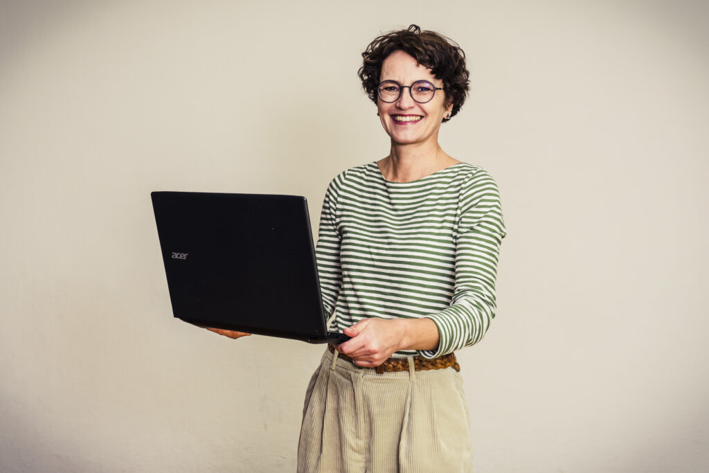 Unternehmensblog führen: Frau mit Laptop, gutgelaunt