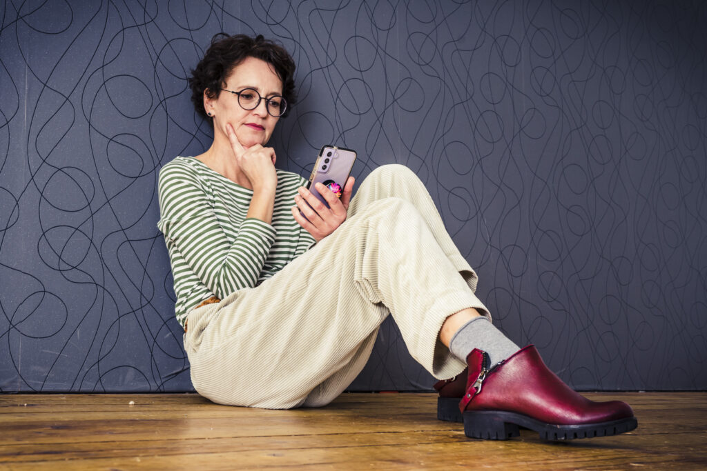 Frau sitzt auf dem Boden und schaut skeptisch auf das Handy