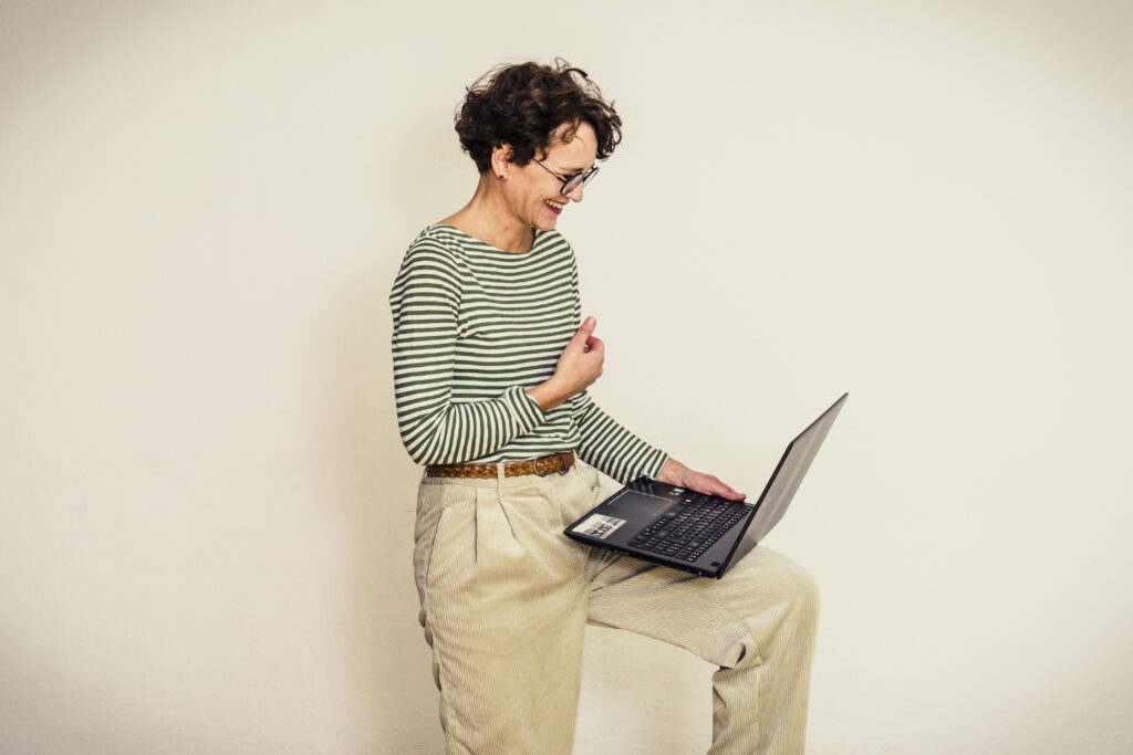 Frau in gestreiftem Shirt blickt fröhlich auf den Laptop