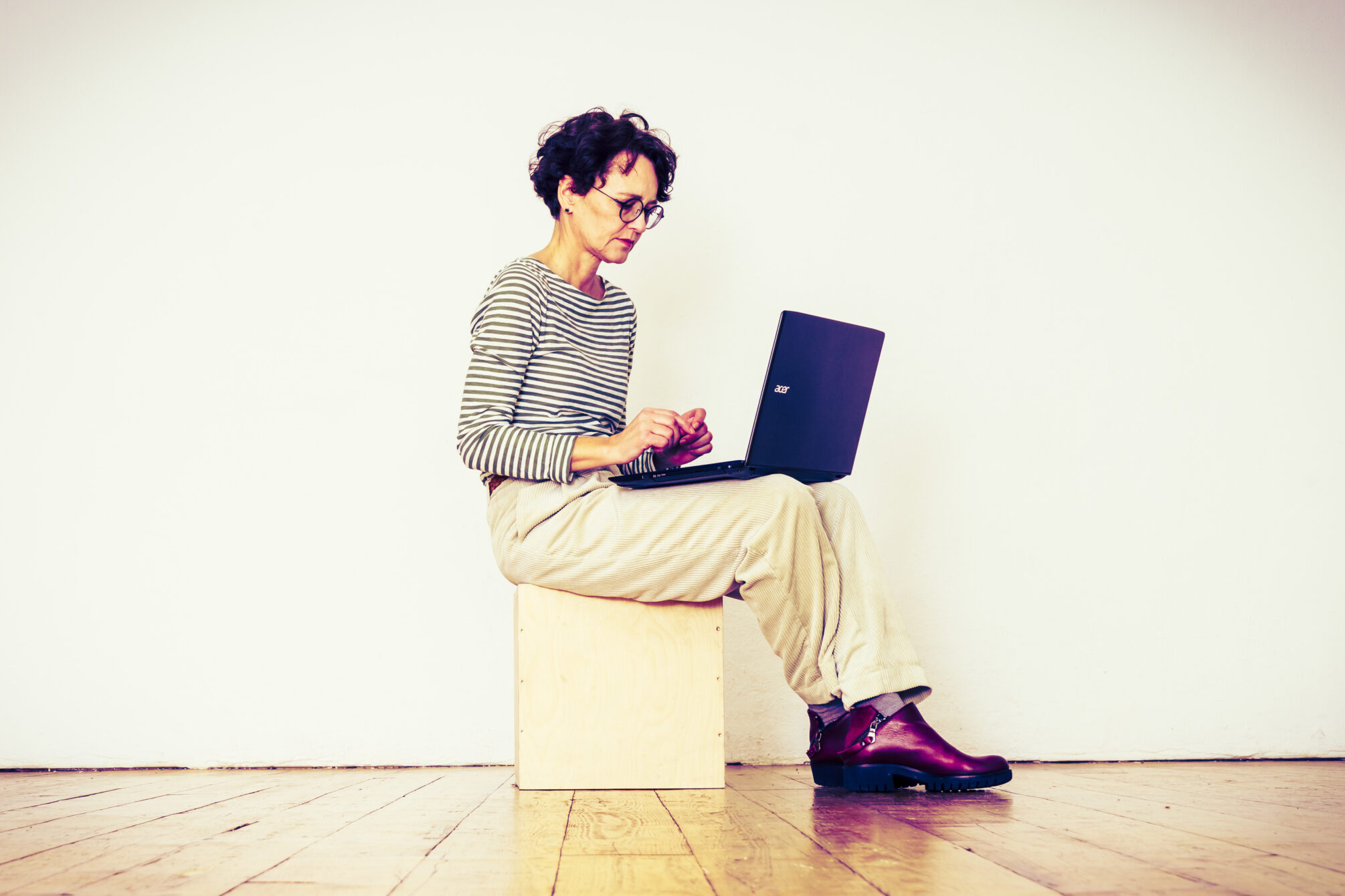 Frau sitzt auf einem Hocker mit dem Laptop auf den Beinen und Arbeitet