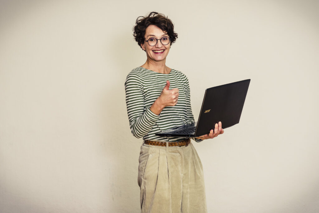 Blog Post schreiben und aufbauen: Frau blickt mit Laptop und Daumen hoch in die Kamera