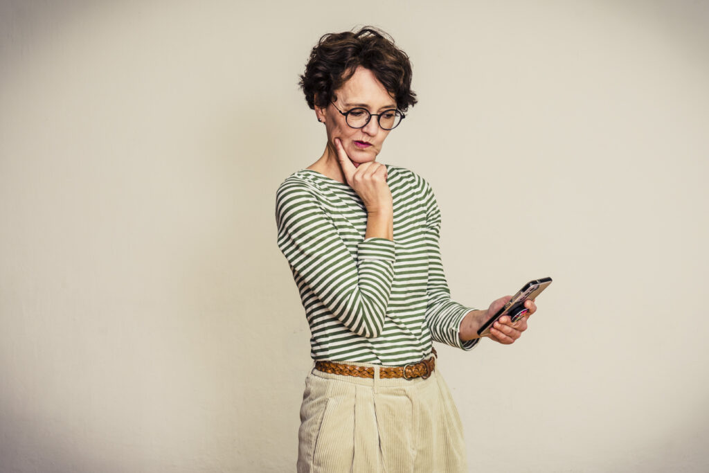 Frau in gestreiftem Shirt blickt skeptisch auf das Handy