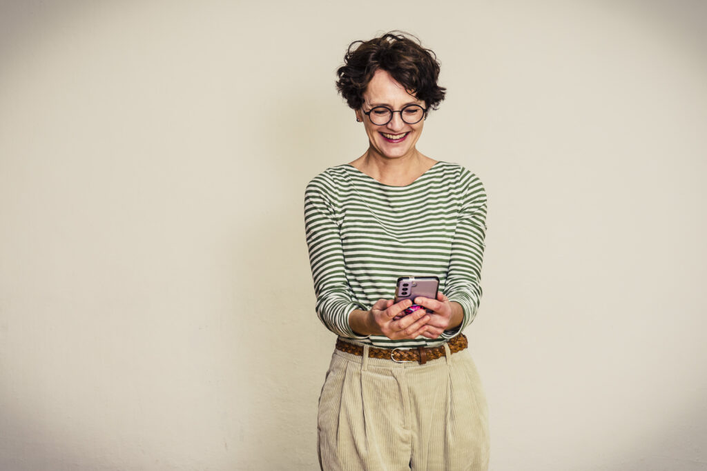 Keywords finden: Frau in grüngestreiftem Shirt blickt fröhlich auf das Handy